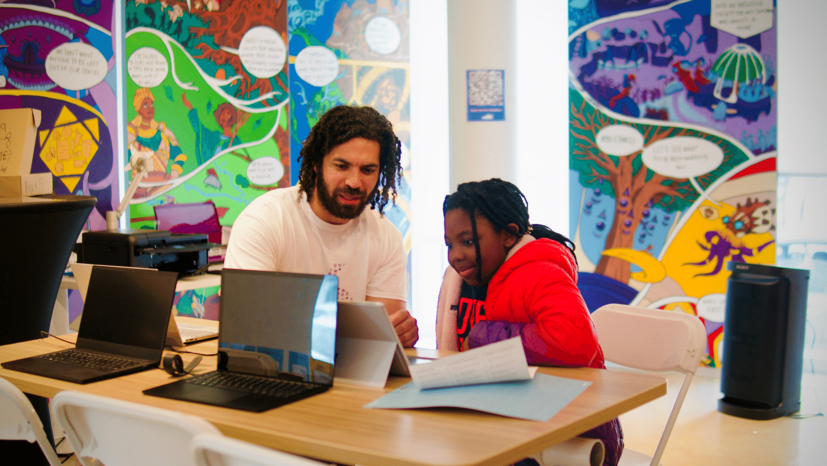 Facilitator Nigel works with a youth over a laptop at the grand opening launch event
